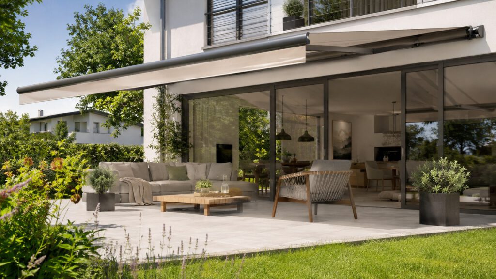 Eine Markise spendet Schatten auf der Terrasse und schützt angrenzende Glasflächen